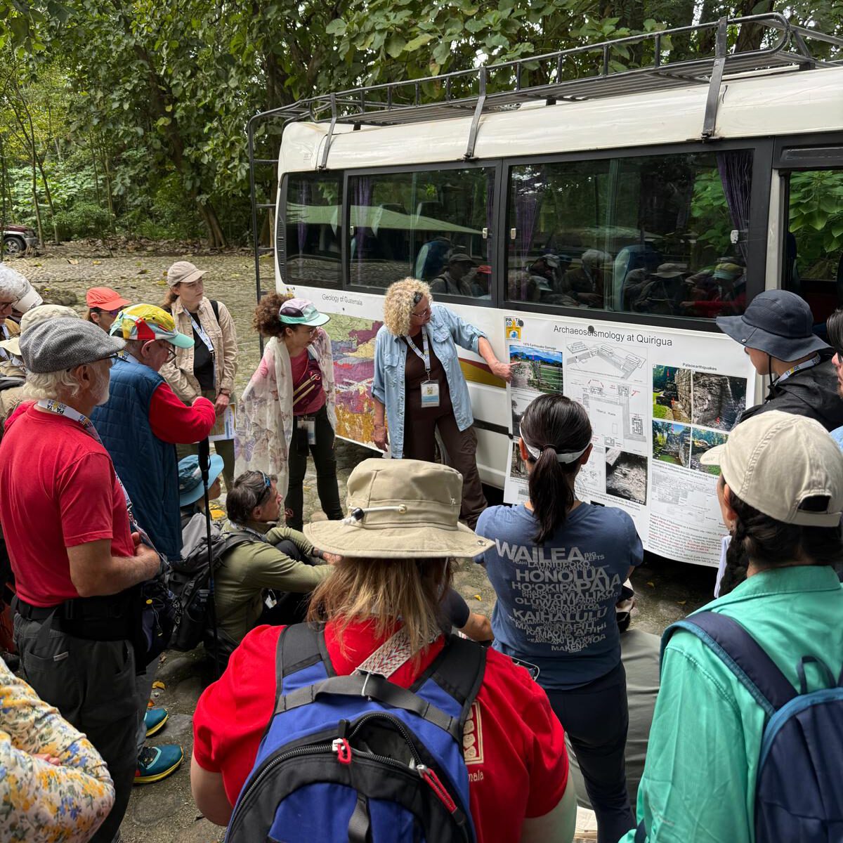a scientist explaining geology using a map that's fixed to the side of a bus, people surrounding her