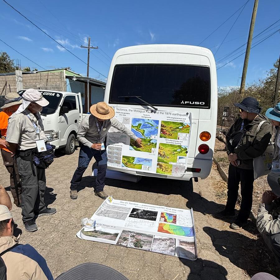 a scientist explaining geology using a map that's fixed to the side of a bus, people surrounding him